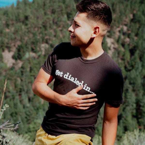 a man is posing, wearing a black "get dialed in..." T-shirt