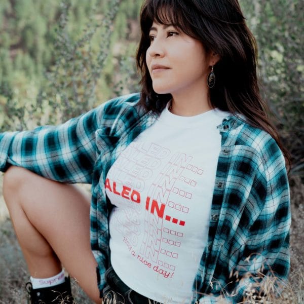 a woman is posing, wearing a white "Thank You Very Much" T-shirt